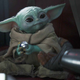 Baby Yoda aka Grogu holds onto a silver ball while sitting in a spaceship.